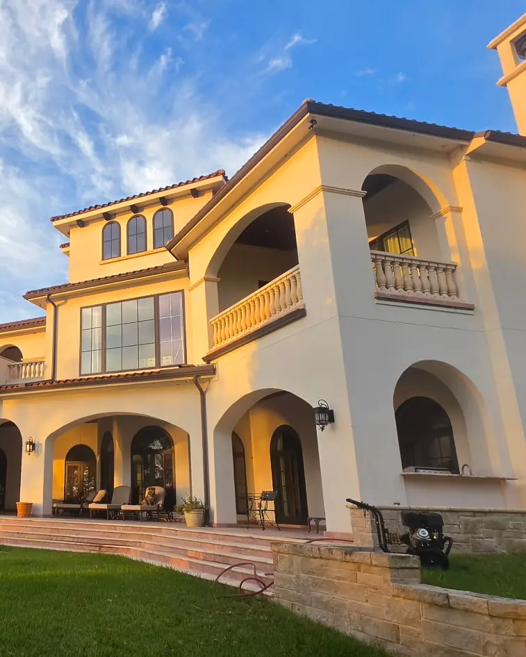Two-story stucco home with arched balconies and a tower, photographed at sunset