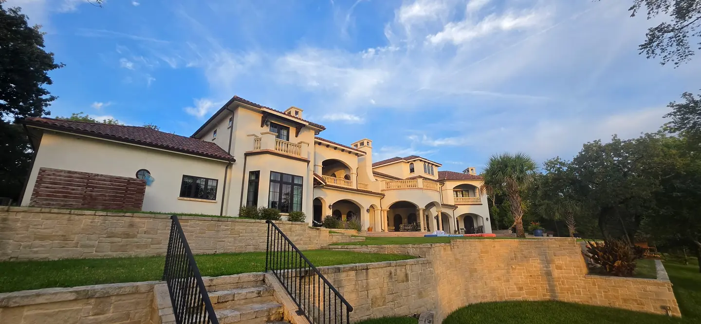 Terraced stone patio with steps and iron railings below a large stucco home