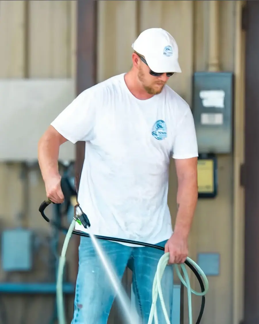 Man in a white 6L Power Washing T-shirt and cap holding a spray gun and hose