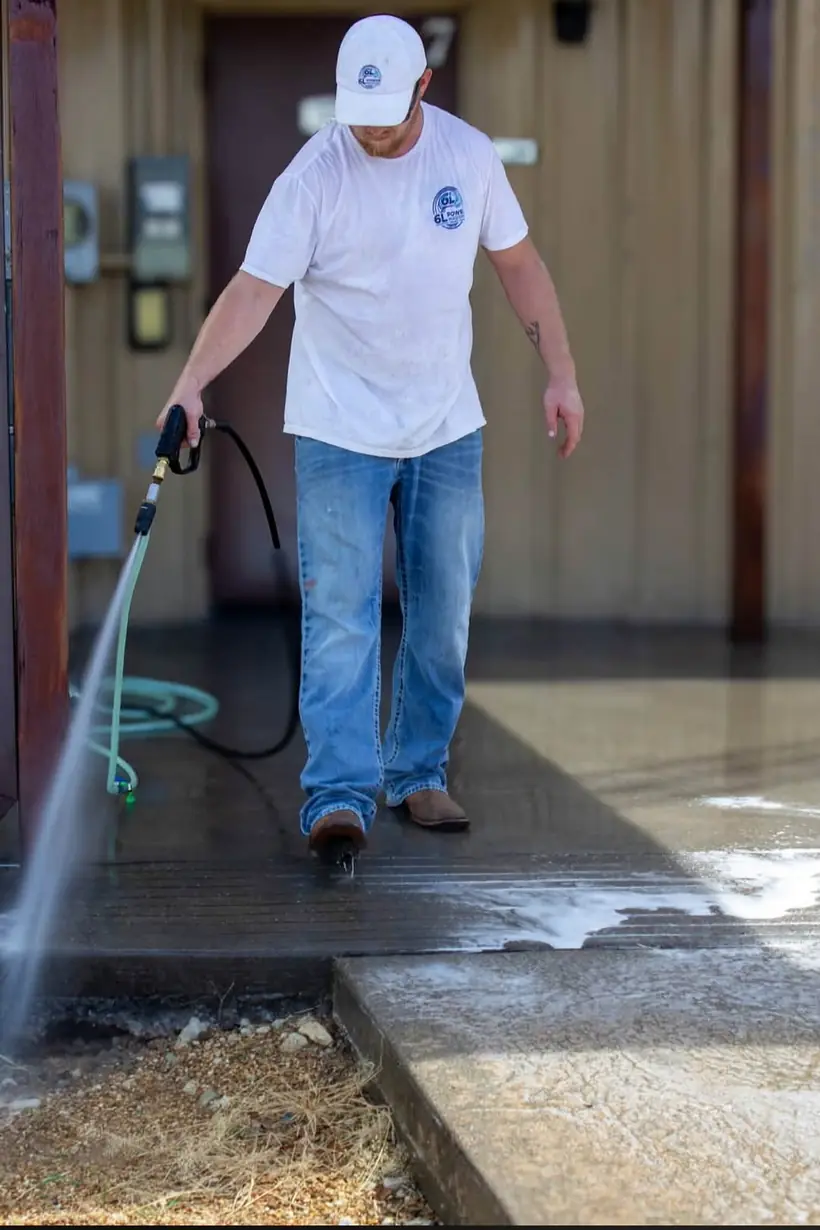 Rinsing a concrete walkway under a covered porch with a pressure washer wand